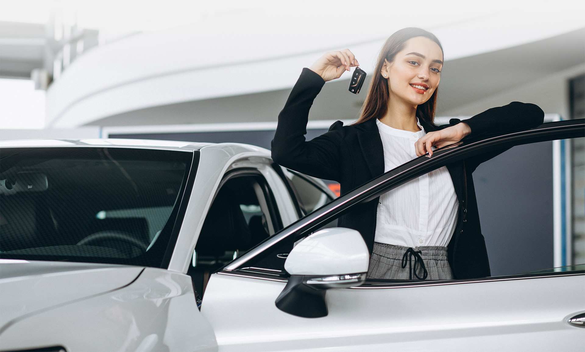 Young woman standing beside open car door holding keys